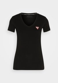 T-shirt noir manches courtes pour femme avec col en V et petit logo Guess rouge et blanc sur le côté gauche de la poitrine.