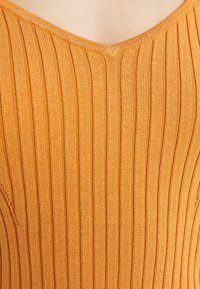 Gros plan sur un vêtement en maille orange côtelé avec un décolleté en V sur une peau claire.