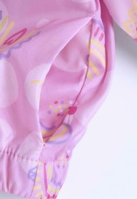 Tissu rose avec des motifs abstraits jaunes et violets, avec des poignets élastiques et une texture douce. Gros plan sur un détail de manche.