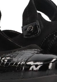 Zapatos cerrados negros con un patrón de reptil texturizado, acentos de ante y una correa ajustable con un detalle de hebilla brillante.