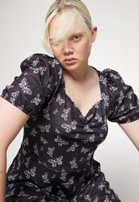 Vestido preto com mangas curtas bufantes, apresentando um padrão de borboletas brancas. Design de decote em V com detalhes de franzido no centro. Textura suave.