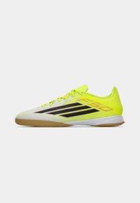 Φωτεινά κίτρινα αθλητικά παπούτσια με υφή στην επάνω επιφάνεια, μαύρες ρίγες και εξωτερική σόλα από καουτσούκ καφέ χρώματος. Σχεδιασμός με χαμηλό προφίλ και κλείσιμο με κορδόνια.