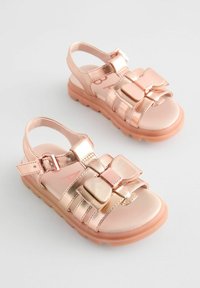 Roze gouden sandalen met verstelbare gespen, platte rubberen zolen en een strikaccent. Glad oppervlak met een metallic afwerking en een open achterkant.