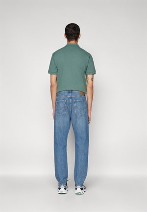 Green polo shirt with short sleeves, paired with light blue relaxed-fit jeans. White sneakers with multi-colored accents.