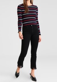 Mörkblå långärmad topp med vita och röda ränder, ihop med höga svarta jeans med fransade nederkantar och spetsiga svarta klackar.