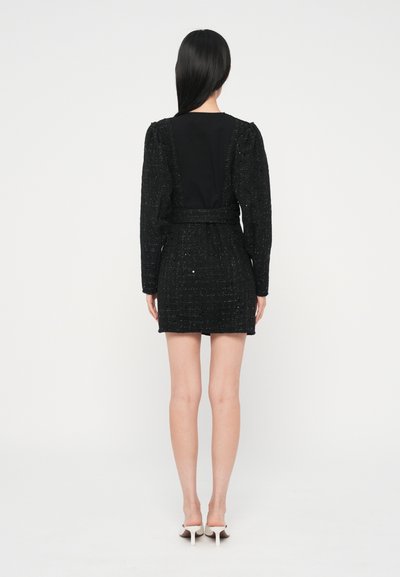 Melns tvida kleita ar garām pūkainām piedurknēm un piegulošu vidukli. Gluda melna muguras daļa. Īss hemline. Valdīta ar baltām papēžu muleēm.