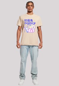 Beige cotton t-shirt featuring colorful cartoon print of food with text. Paired with light blue denim jeans and white sneakers.