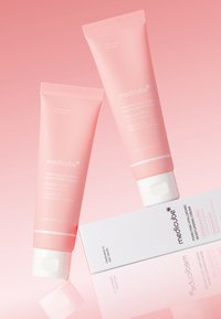 Dwa różowe tubki kremu nawilżającego Medicube PDN Pink Hyaluronic są ustawione pod kątem na powierzchni lustrzanej, a częściowo widoczny jest biały prostokątny pudełko.