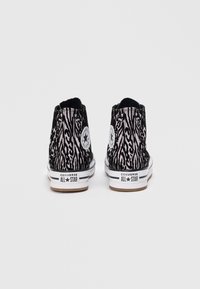 Augstas tenisēšanas kurpes ar melnu un rozā zebra rakstu, baltu gumijas zoli un Converse All Star logo uzlikumu uz papēža.