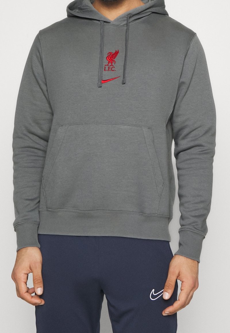 Sweat à capuche gris en tissu lisse avec une poche kangourou. Présente un logo brodé rouge de Liverpool FC et un swoosh Nike sur la poitrine.