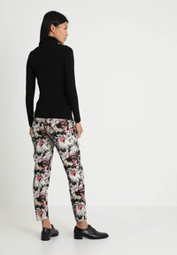 Sort langærmet turtleneck sat sammen med bukser med blomsterprint i sort, pink og hvid, suppleret med sorte sko.
