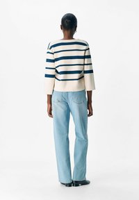 Gestreifter Pullover in Creme und Marineblau, mit Dreiviertelärmel, kombiniert mit hellblauen Jeans und schwarzen Ballerinas, von hinten betrachtet.