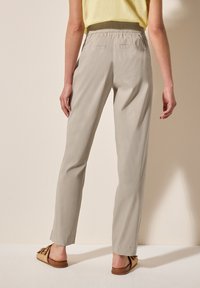 Pantaloni beige chiaro con una vestibilità rilassata. Presentano una vita elastica, tasche laterali e una superficie liscia. Indossati con sandali scivolati marroni.