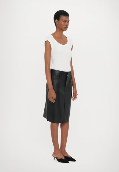 White short-sleeve top, black leather skirt, knee-length, flat-front design with pockets. Model wears black pointed-toe flats.