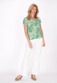 Top verde chiaro a maniche corte con un motivo floreale, abbinato a pantaloni bianchi a gamba larga e scarpe con tacco beige.