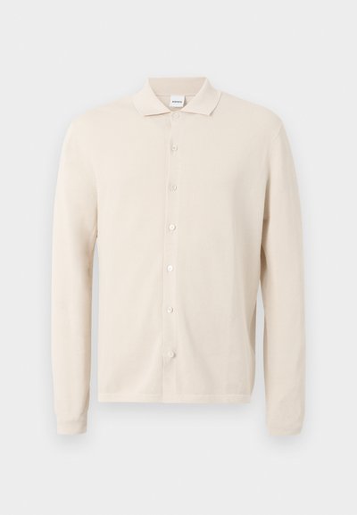 Cardigan beige à manches longues, boutonné devant avec col, tissu texturé, et sept boutons sur le devant, présenté sur un fond clair uni.