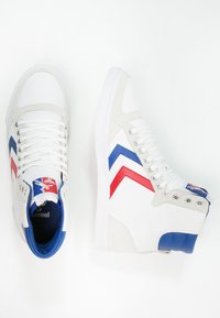 Adidași albi cu glezna înaltă, confecționați din materiale din piele întoarsă și pânză. Accente în nuanțe de albastru și roșu cu un motiv în zigzag și un logo colorat pe limbă. Șireturi albe.