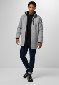 Veste en polaire grise avec un col haut, fermeture éclair, poches latérales et une finition texturée, associée à un jean foncé et des bottes noires chunky.