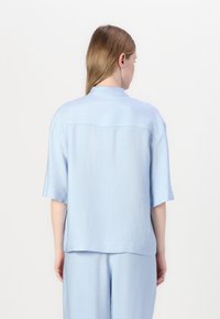 Světle modrý top s krátkým rukávem a texturovaným povrchem, který má zadní klapku a design límce, spárovaný se světle modrými kalhotami.
