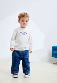 Vitt långärmat skjorta med blå text som lyder "Always Awesome", kombinerad med blå randiga baggyjeans och vita sneakers.