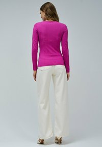Top ajustado de manga larga en material de canalé rosa brillante, combinado con pantalones de pierna ancha blancos y tacones en tonos neutros. Diseño simple, sin patrones.