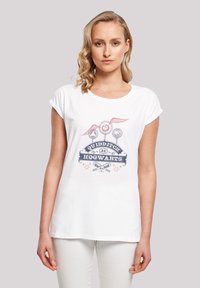 Hvit bomull T-skjorte med rullet ermer, prydet med grafisk design av Quidditch-elementer, inkludert staver, baller og tekst i marineblått og rødt.