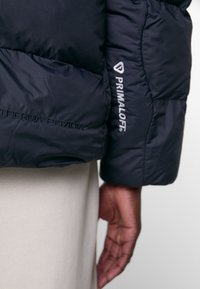 Marinblå vadderad jacka med Therma-FIT och Primaloft-logotyper. Quilted textur med mjukt, isolerande material och figursydd silhuett.