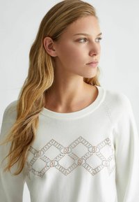 Maglione bianco con scollo rotondo e motivo a rombi realizzato con perline bianche e rosa oro sul petto.
