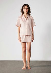 Ljusrosa kortärmad pyjamasett i mjukt tyg, med en knäppbar skjorta och matchande shorts med en enkel fickdetalj.
