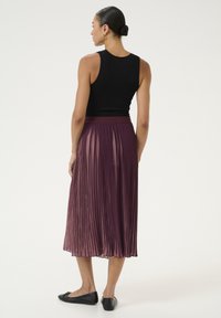 Top a canotta nera a coste abbinata a una gonna plissettata di lunghezza media di un profondo colore viola. Scarpe nere basse completano l'outfit. Tessuto morbido e fluido.