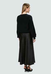 Schwarzer Strickpullover, entspannter Schnitt, kombiniert mit einem schwarzen Satin-Maxikleid. Der Rock hat eine glatte Textur und ein fließendes Design.