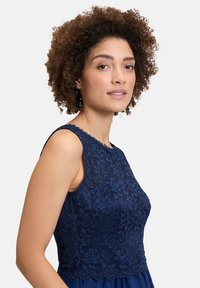 Tengerészkék csipkés ruha, kerek nyakkivágással, virágmintákkal és struktúrált felsőrészével, sima szoknyába folyik át.