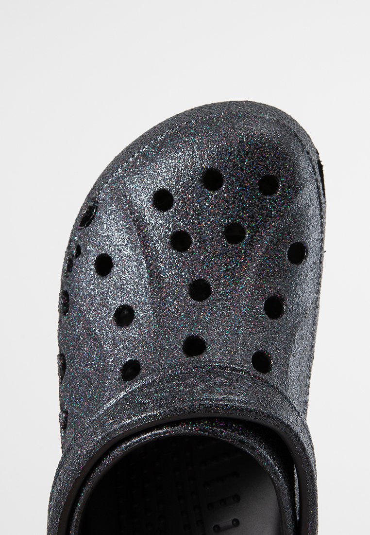 Schwarze Glitzer-Clogs mit einer strukturierten Oberfläche, die mehrere Belüftungsöffnungen, eine konturierte Form und einen Fersenriemen für einen sicheren Sitz aufweisen.