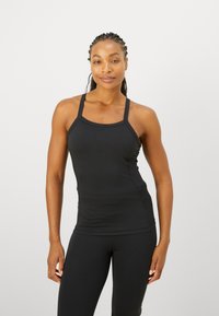 Črn športni top z tankimi naramnicami, prilega se in ima gladko teksturo, v kombinaciji z usklajenimi legginsami. Preprost in minimalističen stil.