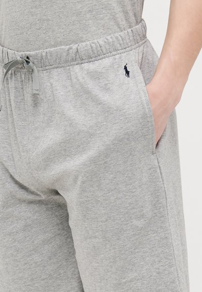 Šedé bavlnené tepláky s elastickým pásom, detailom na šnúrku, bočnými vreckami a malým tmavým logom na ľavej strane.