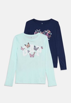 Deux chemises à manches longues, une bleu clair avec GAP et des papillons roses, une marine avec un groupe multicolore de papillons sur la poitrine.