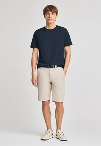 T-shirt en coton bleu marine, shorts beiges et baskets beiges. La T-shirt présente un petit logo ; les shorts ont des poches et une coupe décontractée.