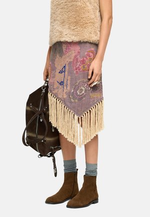 Spódnica z frędzlami w stonowanym fioletowym kolorze z kolorowymi wzorami; w połączeniu z brązowymi zamszowymi botkami za kostkę i brązową torebką. Widoczne szare skarpetki.