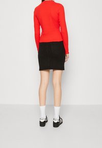 Rotes Langarmoberteil mit gewelltem Saum, kombiniert mit einem schwarzen Jeansrock. Weiße Socken und schwarze Schuhe mit auffälligen Akzenten runden das Outfit ab.