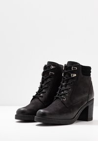 Botines negros de cuero texturizado, con un alto tacón cuadrado, diseño con cordones y ojales metálicos. Punta lisa y collar con acolchado.