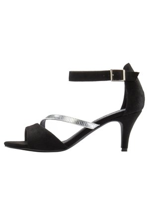 Schwarze Wildleder-Pumps mit hohem Absatz, ausgestattet mit einem strukturierten silbernen Riemen, offener Zehenpartie und verstellbarem Knöchelverschluss. Geschwungene Absatzform mit glatter Sohle.