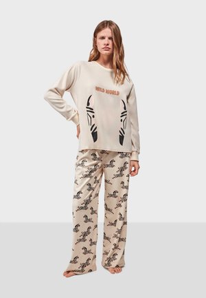 El conjunto de ropa de lounge de color crema cuenta con una blusa de manga larga con estampados de cebra y el texto "WILD WORLD", combinado con pantalones de pierna ancha con estampado.