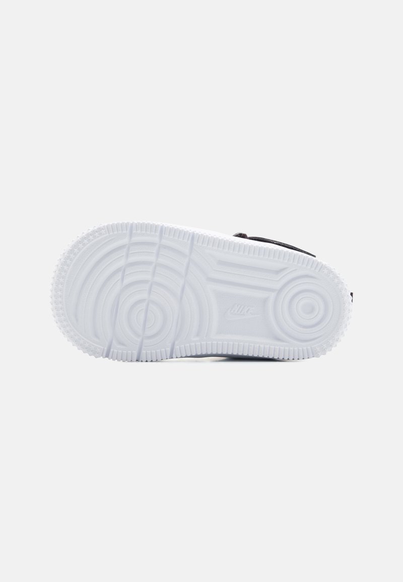 Semelle de sneaker noire avec caoutchouc blanc, présentant des dessins de treads circulaires et des motifs texturés, incluant un logo près du talon.