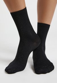 Schwarze Knöchelsocken aus dehnbarem Stoff mit glitzernder Textur. Sie verfügen über einen gerippten Bund und eine glatte Oberfläche.