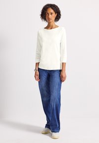 Haut blanc à manches longues avec un décolleté bateau, associé à un jean large bleu et des chaussures de sport blanches. Tissu lisse, design simple, sans motifs.