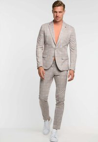 Grijs geruit pak met oranje lijnen, witte shirt en witte sneakers. Slanke pasvorm met twee zakken op de blazer en op maat gemaakte broek.