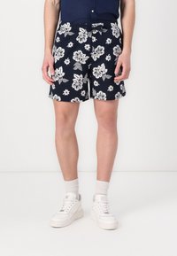 Marineblå shorts med hvitt blomstermønster, laget av lett stoff. L�øs passform, elastisk midjebånd, brukt med hvite joggesko og sokker.