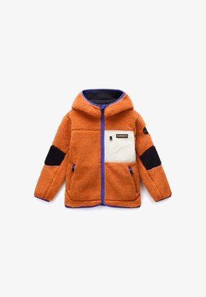 Sherpa jakna u narančastoj boji s mornarskom kapuljačom, bijelim džepom na prsima, crnim detaljima na rukavima i plavim patentnim zatvaračem. Ima dva bočna džepa.