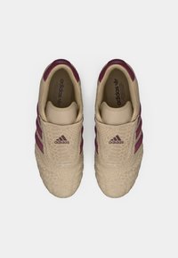 Μπεζ αθλητικά παπούτσια με υφασμένο επάνω μέρος, σκούρες μωβ ρίγες και σχεδιασμό χωρίς κορδόνια. Διαθέτουν ανάγλυφο μοτίβο και ελάχιστη σήμανση.