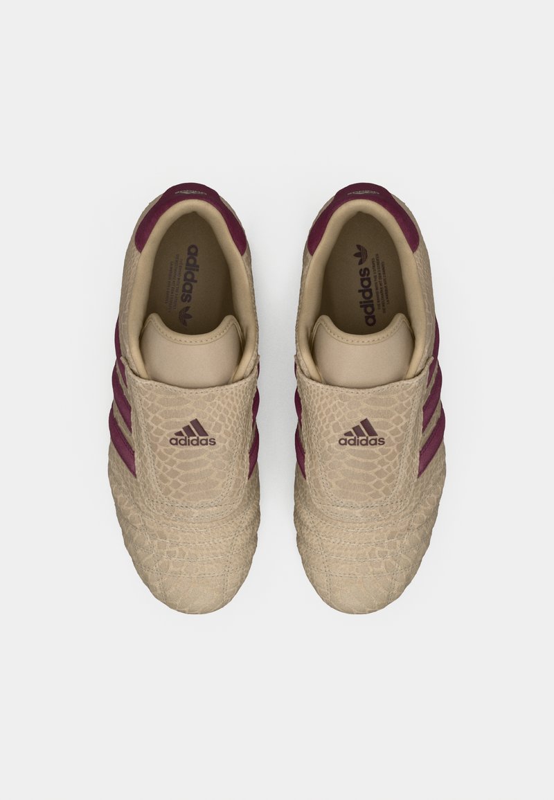 Baskets beiges avec une tige texturée, des rayures violet foncé et un design à enfiler. Elles présentent un motif en relief et un marquage minimal.